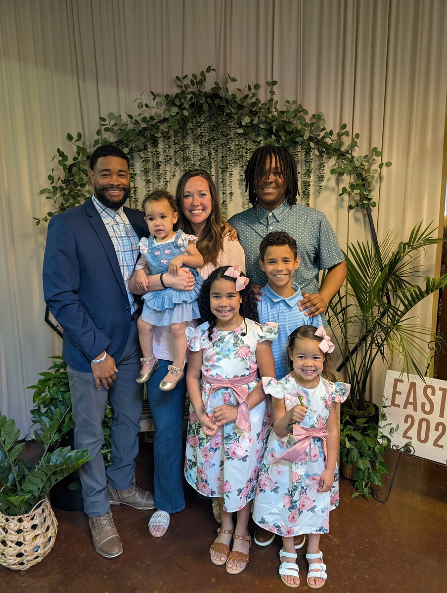 Cameron with his family dressed up for Easter in front of a greenery arch